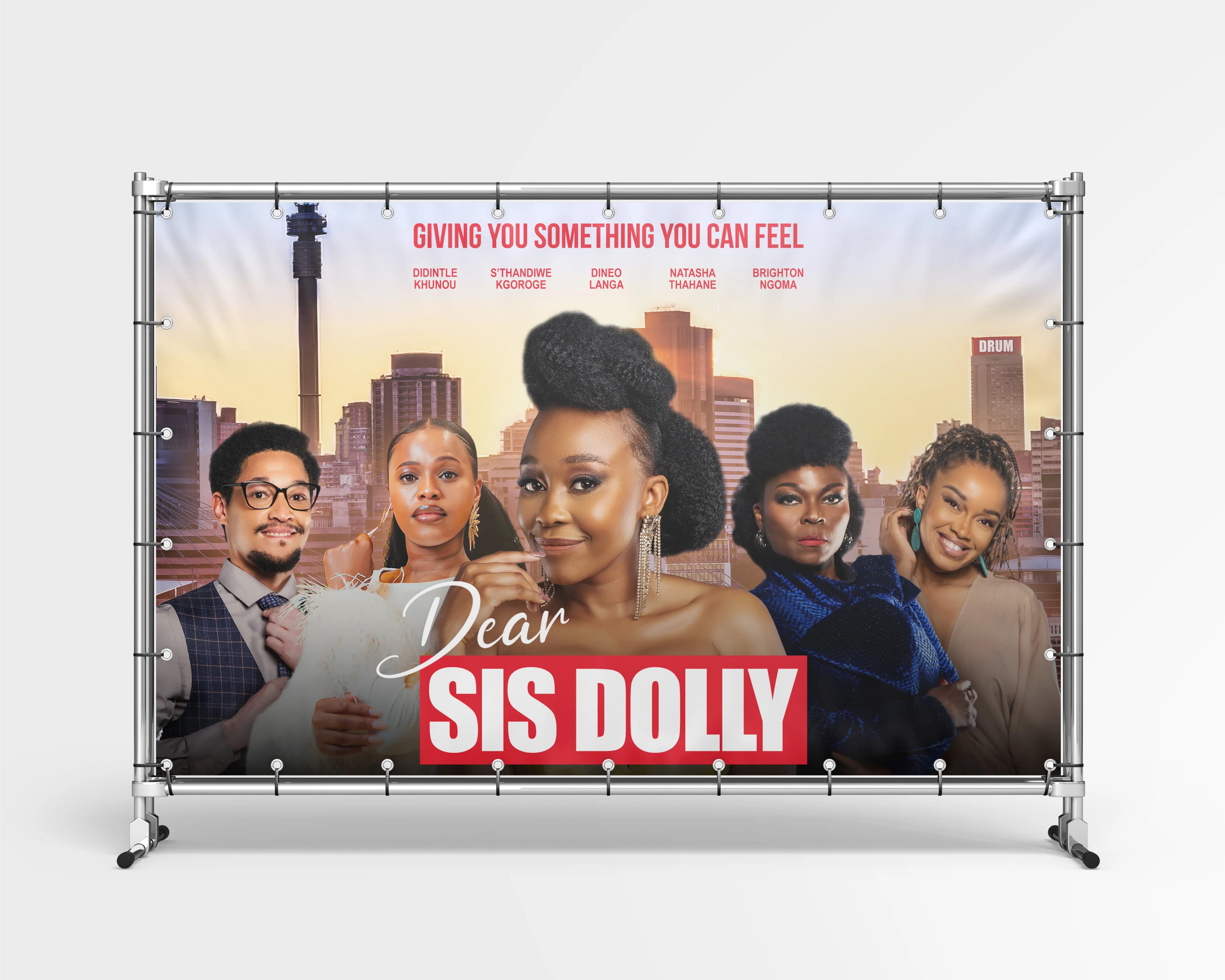 Dear Sis Dolly media wall presented on a portable banner frame, showing five cast members in front of the Johannesburg skyline beside the film logo.
